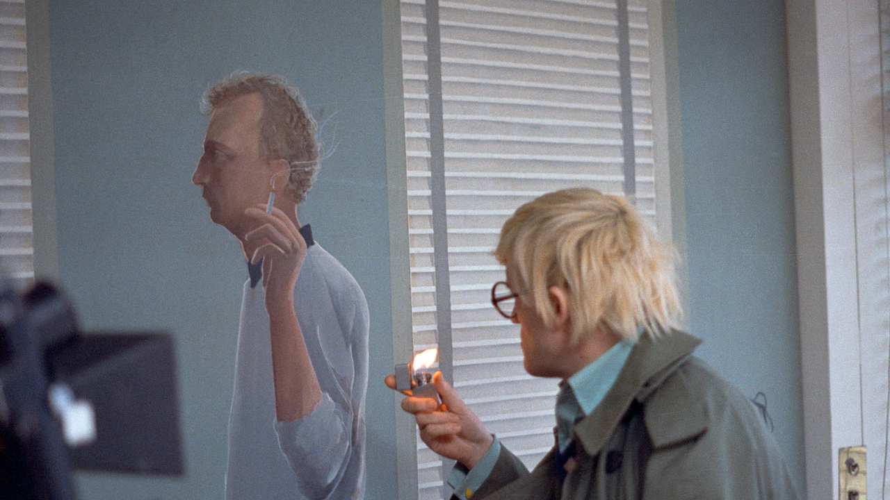 Hockney holding a lighter in front of a painting